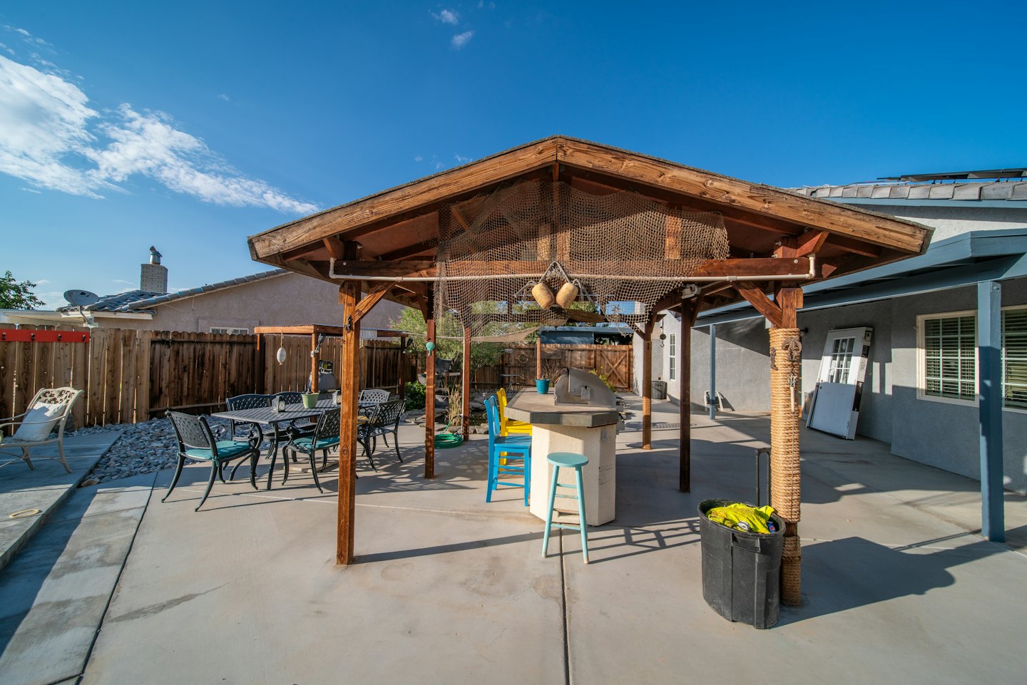 Barra de patio exterior con barbacoa bajo una pérgola junto a un juego de comedor.