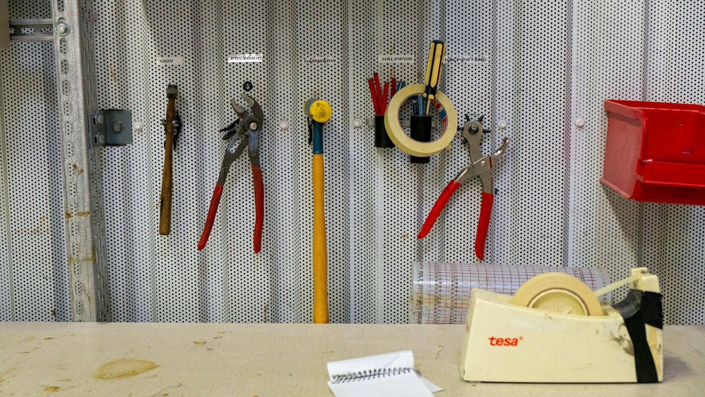 Herramientas de mano ordenadas en un tablero perforado sobre un banco de trabajo de artesanía.