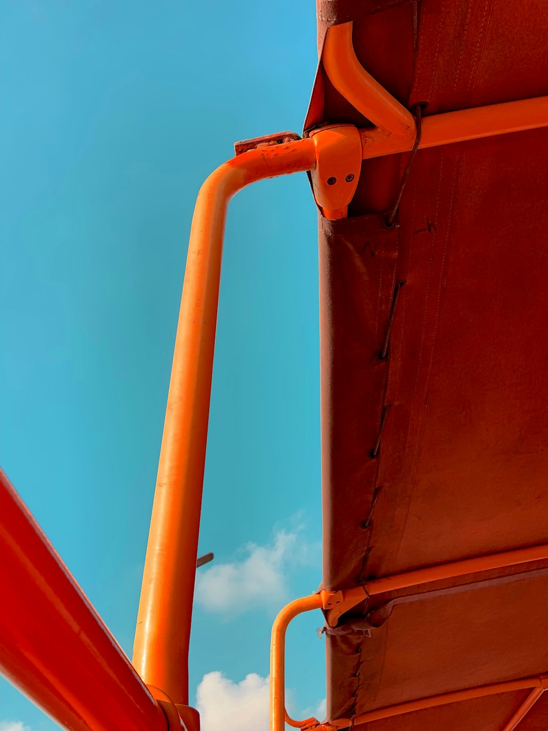 Estructura de toldo de metal naranja contra un cielo azul claro.
