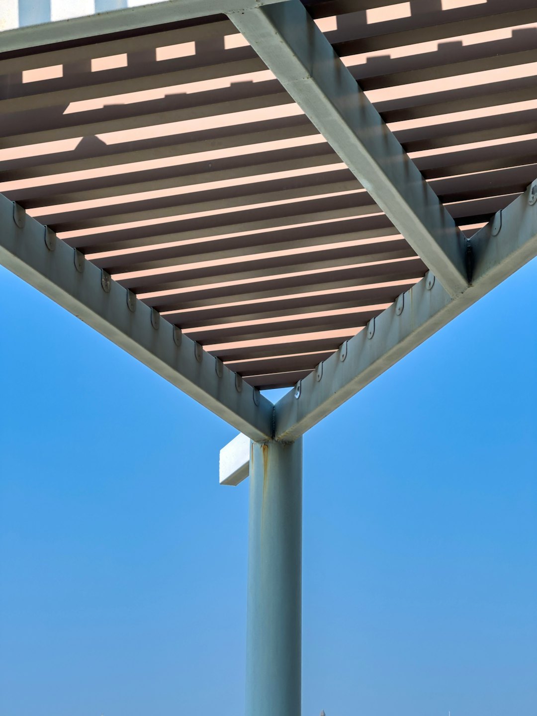 Pérgola moderna de metal con lamas beige se alza contra un cielo despejado.