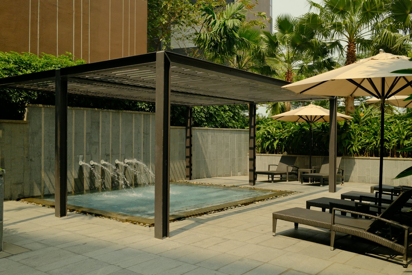 Piscina de resort con chorros de agua bajo una pérgola de metal oscuro.