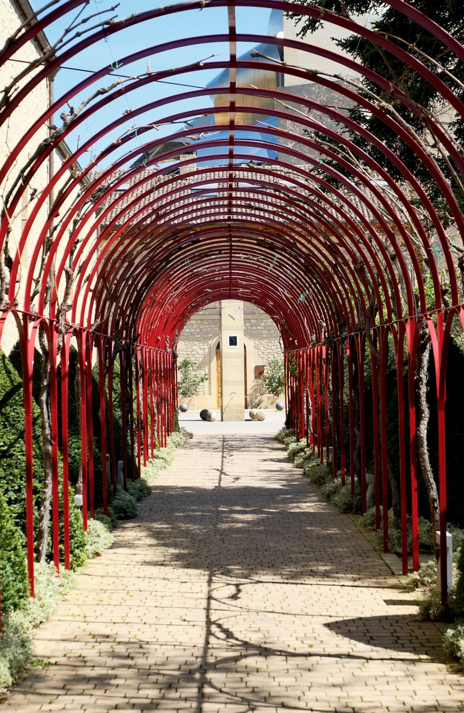 Una pérgola de metal roja se arquea sobre un camino de jardín de ladrillos.