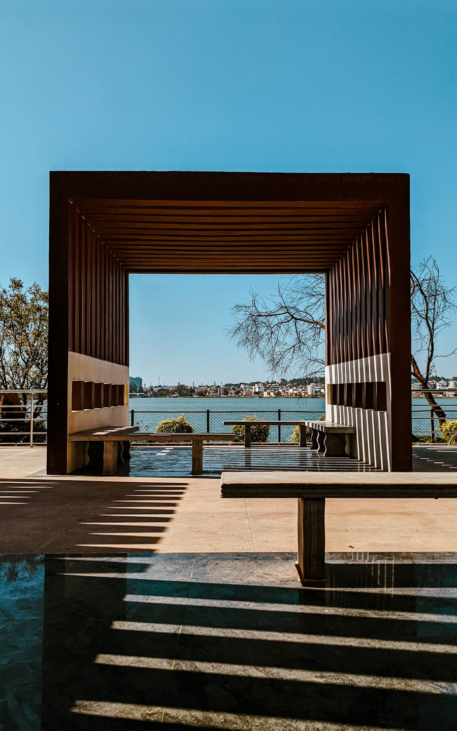Pérgola de madera y bancos de hormigón con vistas al agua y a la ciudad.