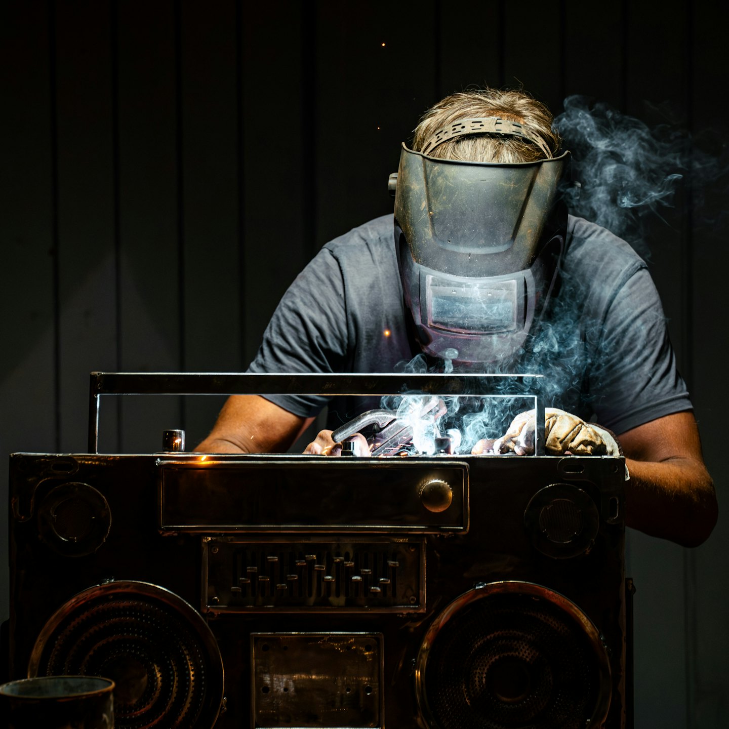 Soldador con máscara y guantes crea una estructura metálica de boombox.